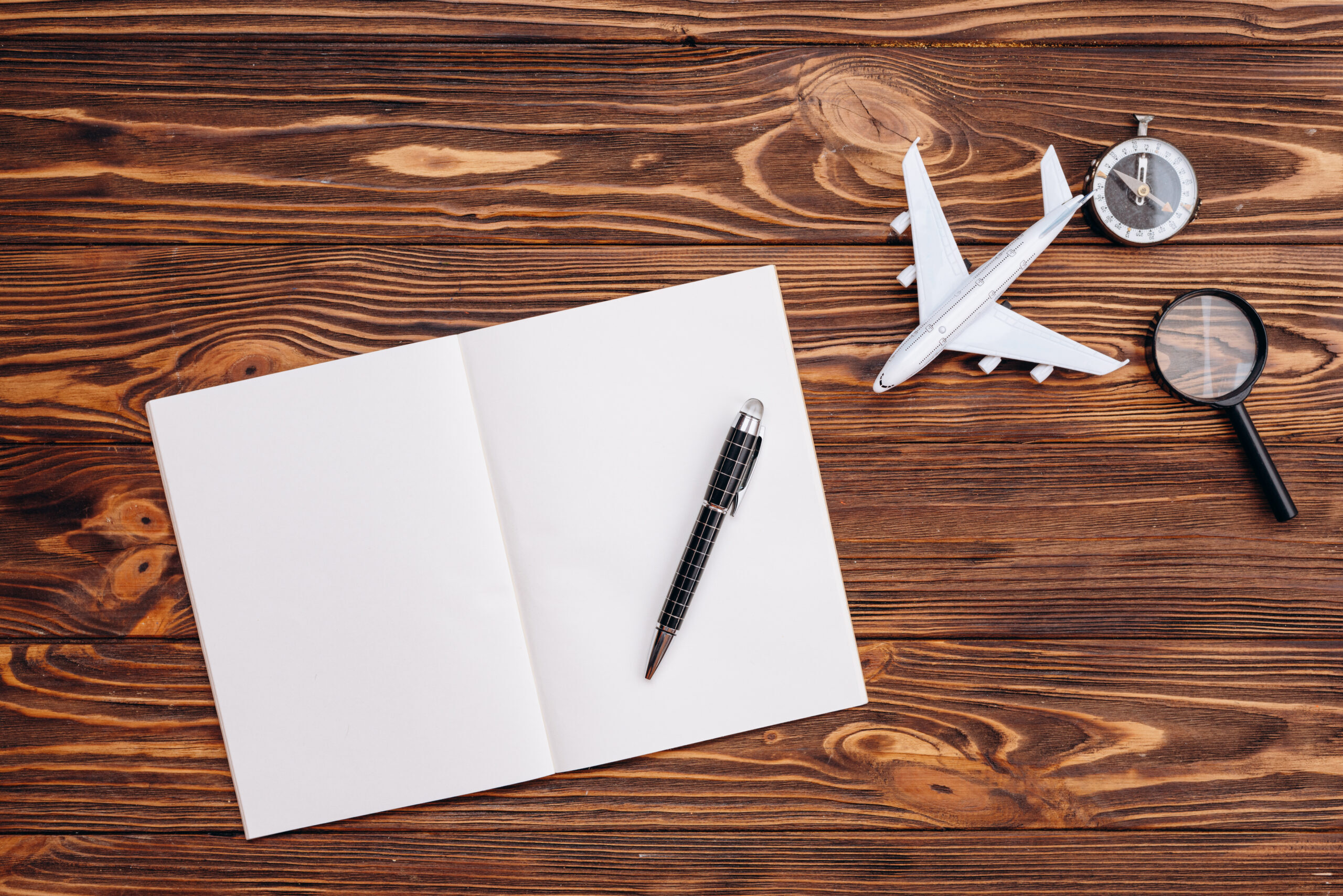 On a wooden surface a blank sheet of paper and a pen, an airplane and a compass, travel concept